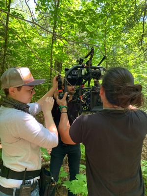 Camera operators filming in lush green forest setting.
