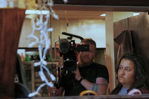 Camera operator filming scene through doorway in dim lighting.