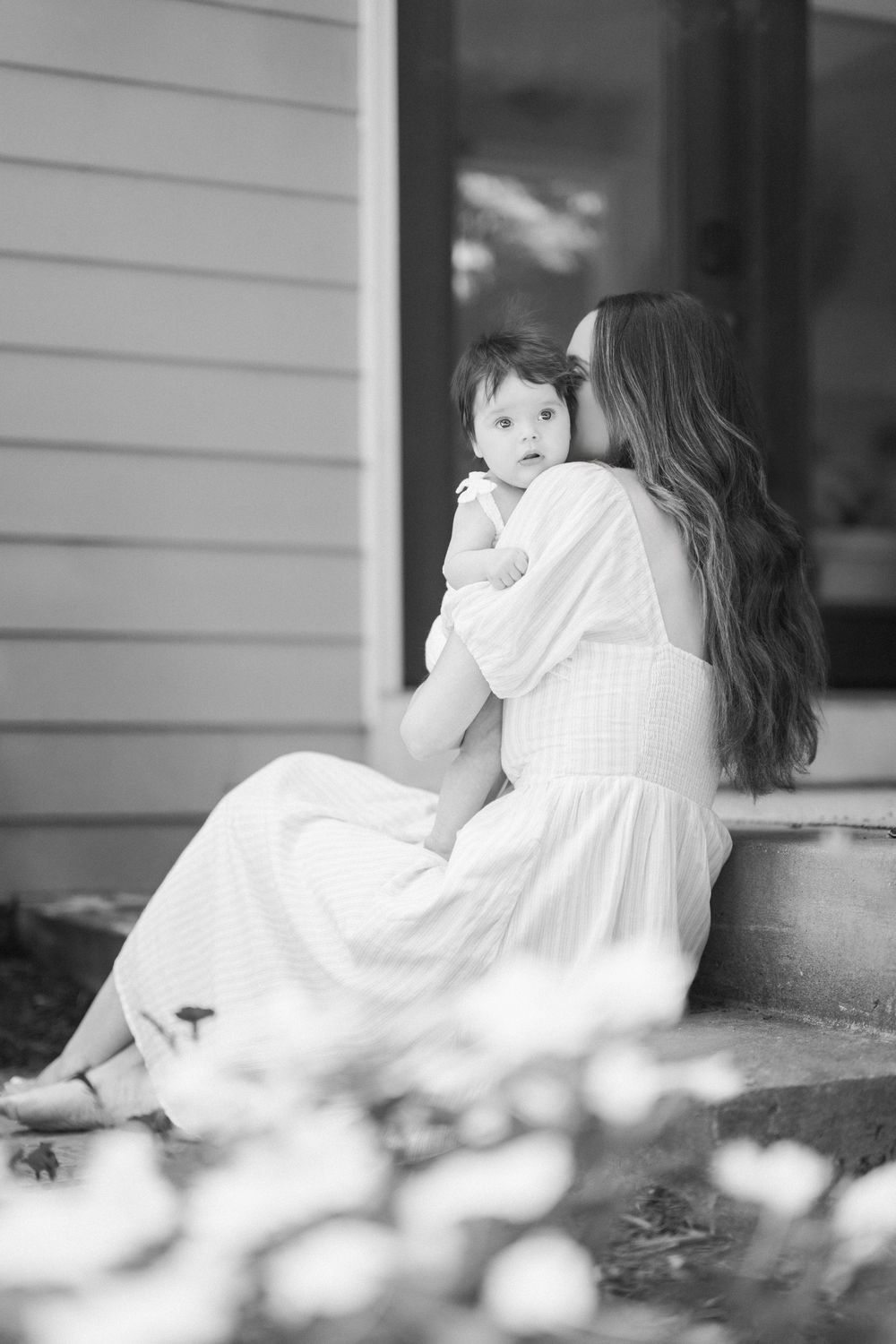 Black and white photo of a mother in a white dress holding her baby on porch steps.