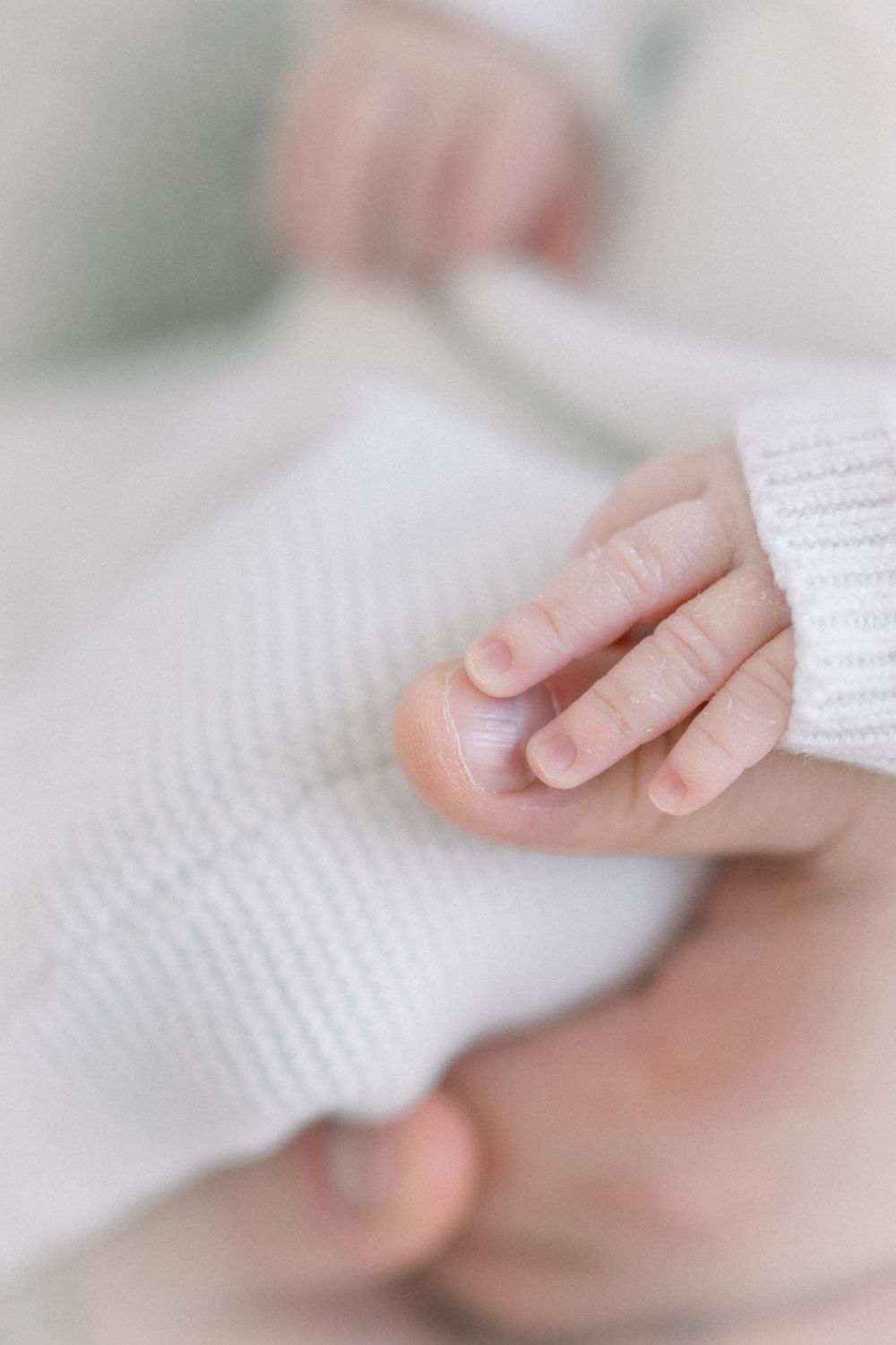 Close-up of a newborn baby's tiny delicate hand resting on a soft white knit blanket.