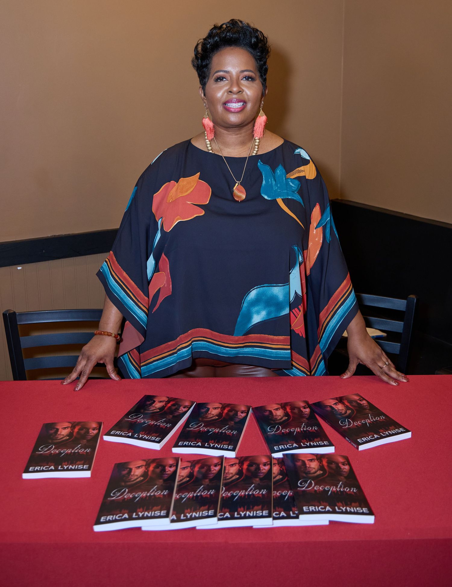 Author sits at table with display of books arranged for signing event.