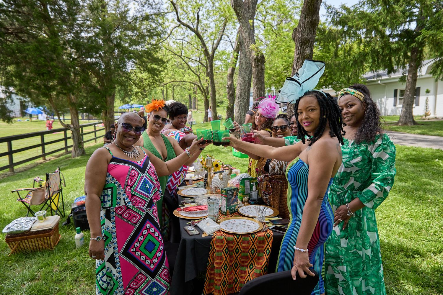 Outdoor gathering with people enjoying food and drinks in green park setting.