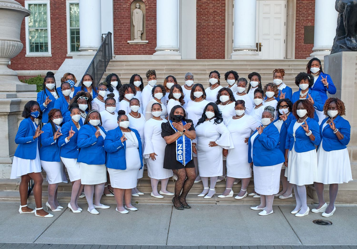 Large group in matching blue and white outfits poses together outside brick building.