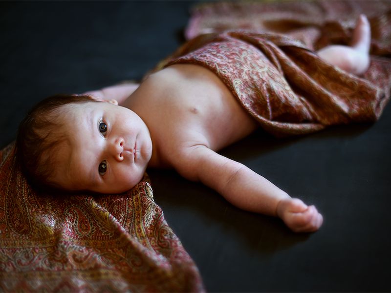 Newborn baby wrapped in a silk scarf, laying on a blanket. Photograph by Abigail's Studio.