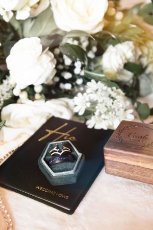 Wedding rings displayed in hexagonal box with white flowers and vows book.