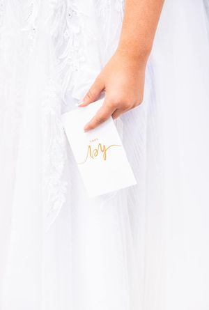 A hand holding a small white card with gold script against a white dress fabric.