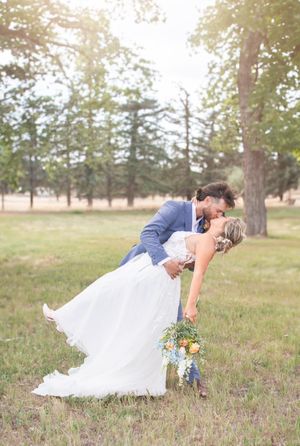 A romantic dip kiss wedding photo in a scenic outdoor setting with pine trees.
