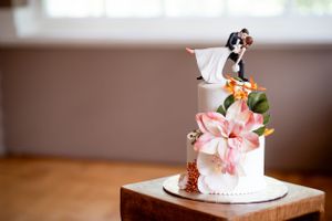 A white wedding cake topped with a bride and groom figurine and pink floral decorations.