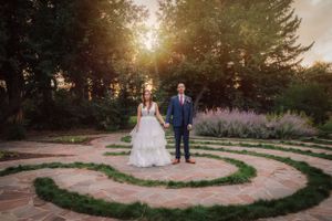 Newlyweds standing on spiral stone pathway in garden during sunset.