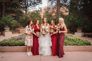 A bridal party in burgundy dresses poses together in a garden setting.