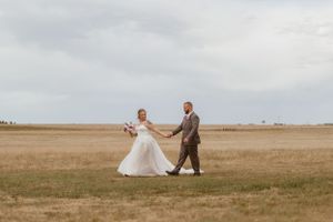 A couple walks hand in hand across a vast open field on their wedding day.