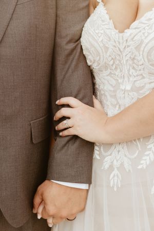 Close-up detail of white lace wedding dress bodice and groom's suit.