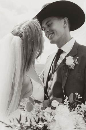 Black and white romantic wedding portrait with cowboy hat and floral bouquet.