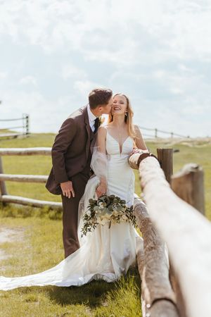Joyful wedding moment by rustic wooden fence with scenic countryside backdrop.