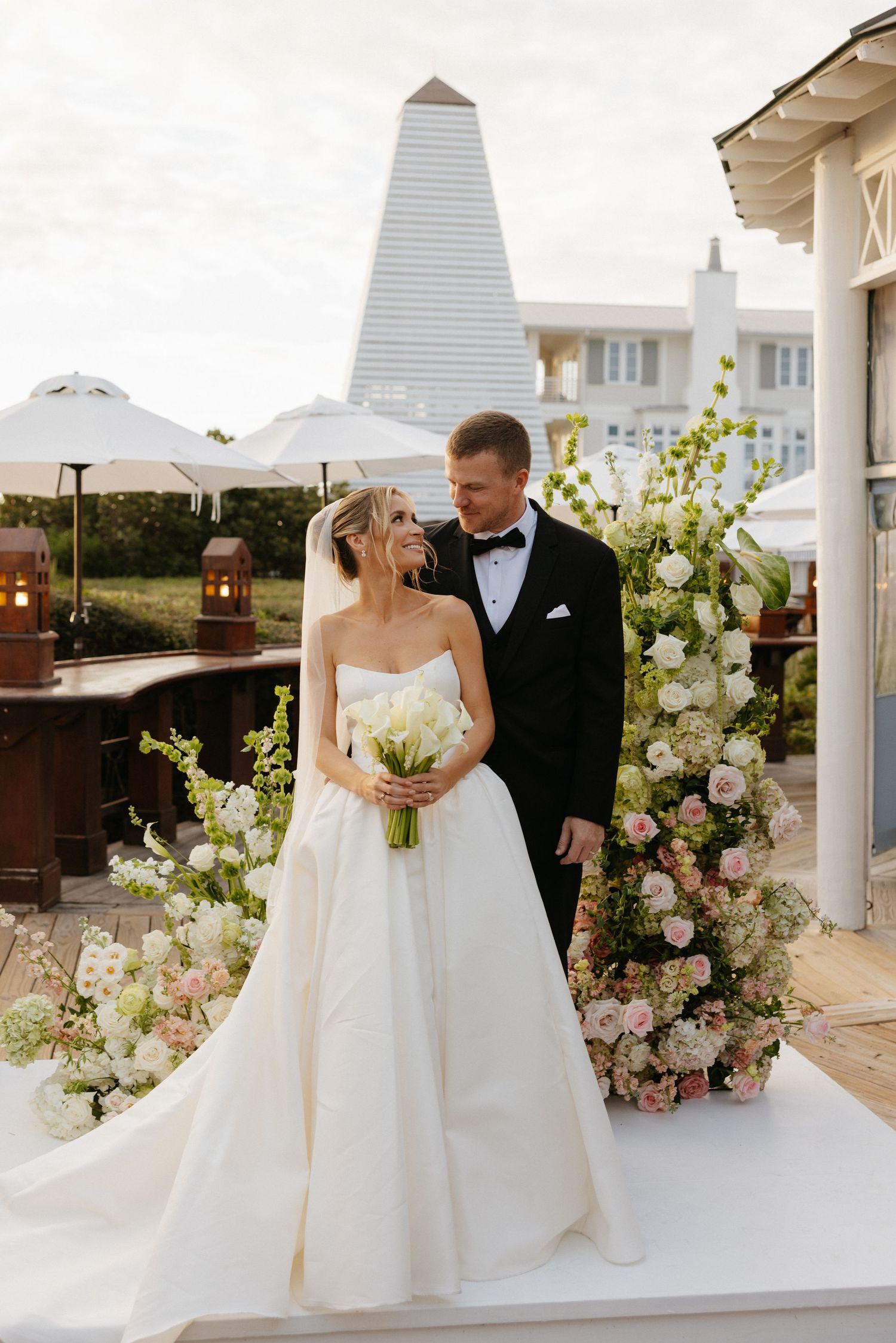 A bride and groom share an intimate moment on a wooden boardwalk at sunset with beach dunes in the background.