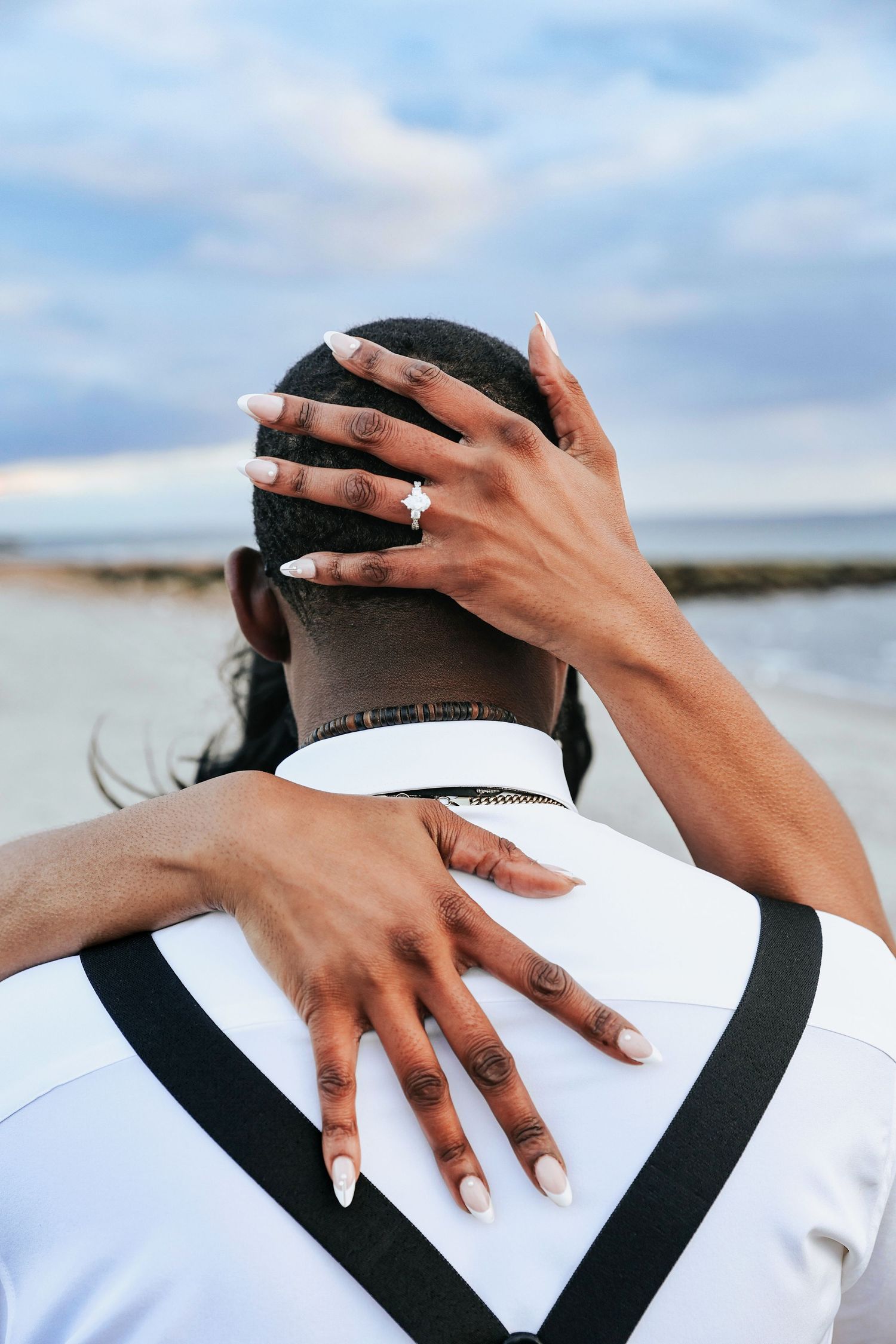 Intimate close-up of hands embracing against blue sky backdrop.