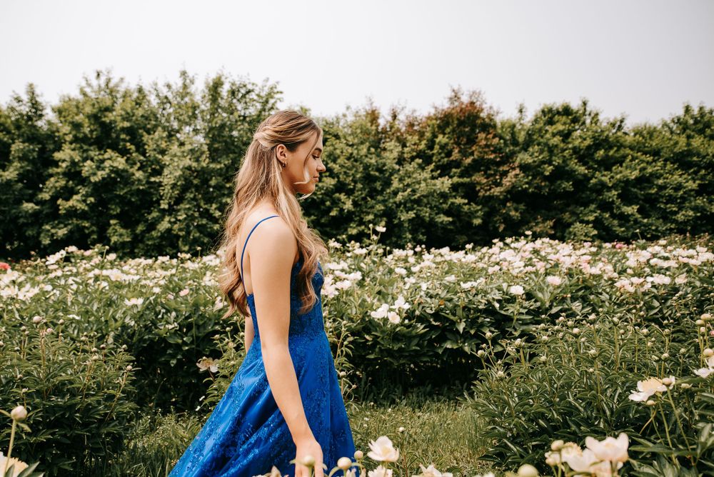 Side profile of person in blue formal gown walking through wildflower field.