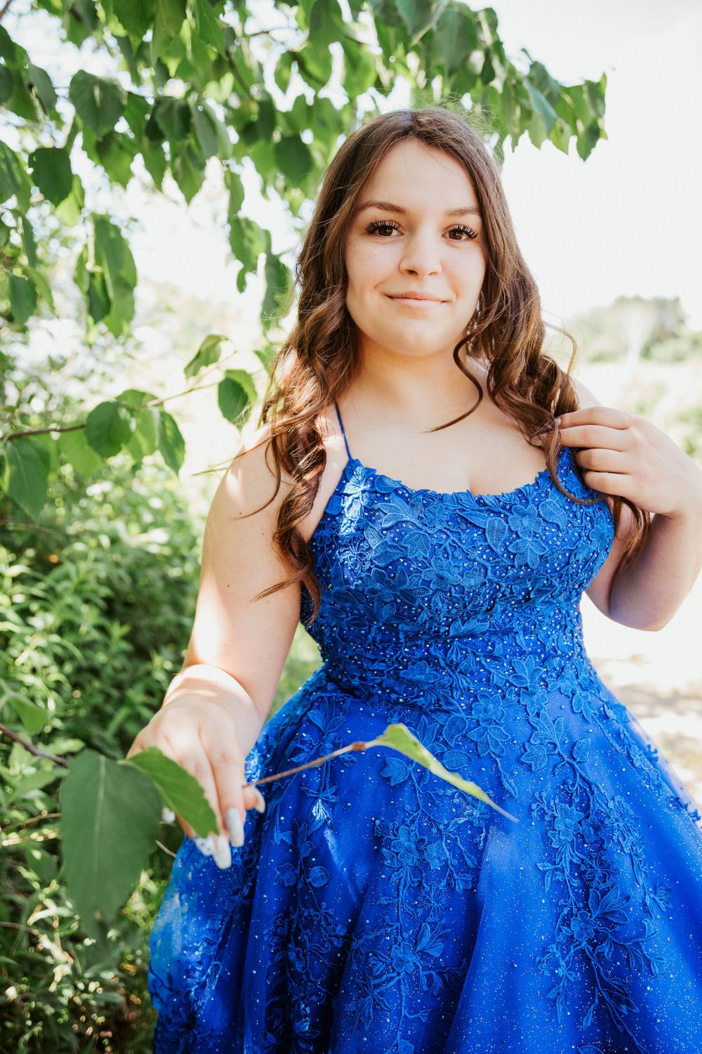 Summer portrait in royal blue lace formal dress among green leaves.