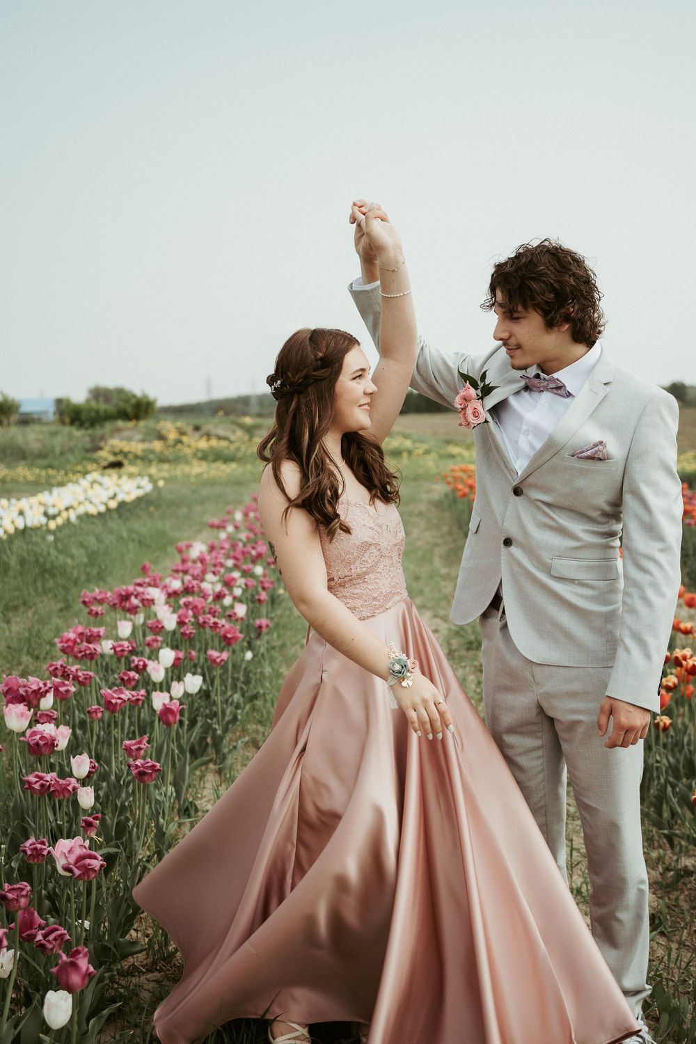 A romantic couple dances together in a blooming tulip field, with the woman wearing a flowing blush pink gown.