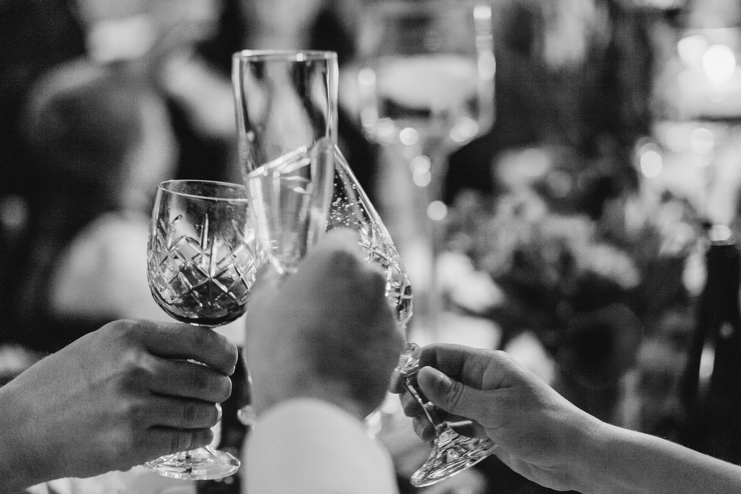 A black and white photo of a group of hands and glasses clinking together for a wedding toast at a New England elopement.