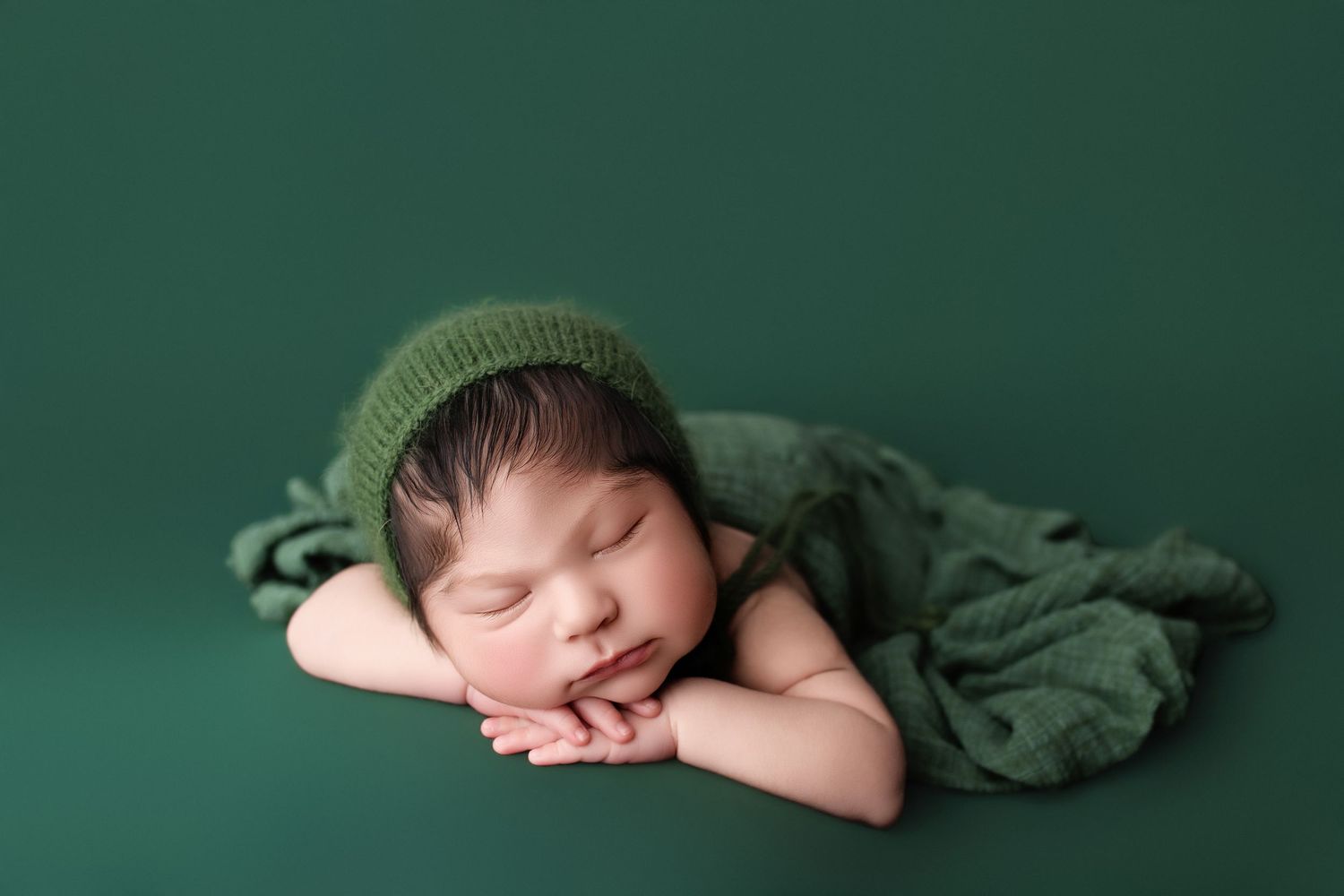 Two sleeping newborns cuddled together on dark blue textured backdrop.