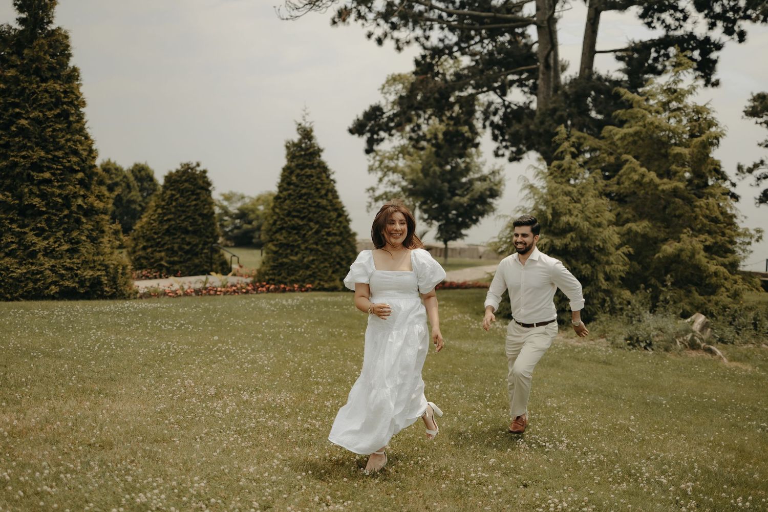 Joyful couple runs through a green garden during their wedding photoshoot.