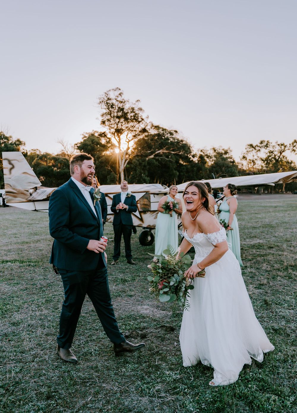 Newlyweds share a playful moment during sunset photo session in open field.