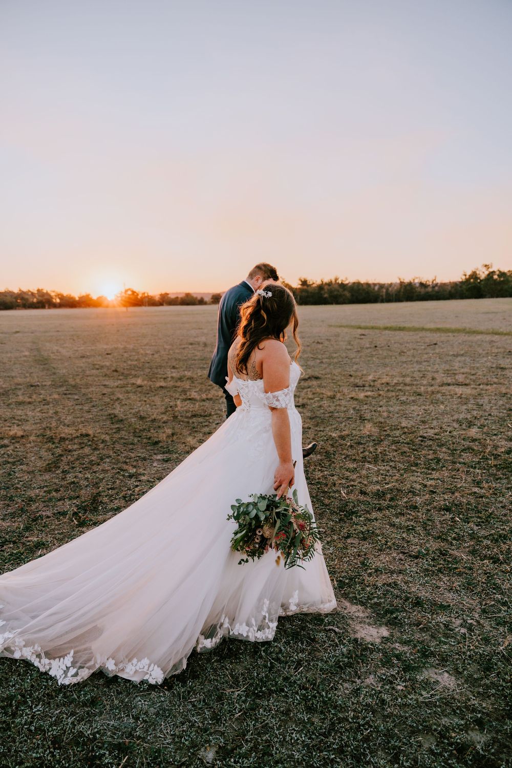 Bride in flowing white dress twirls in an open field at sunset.