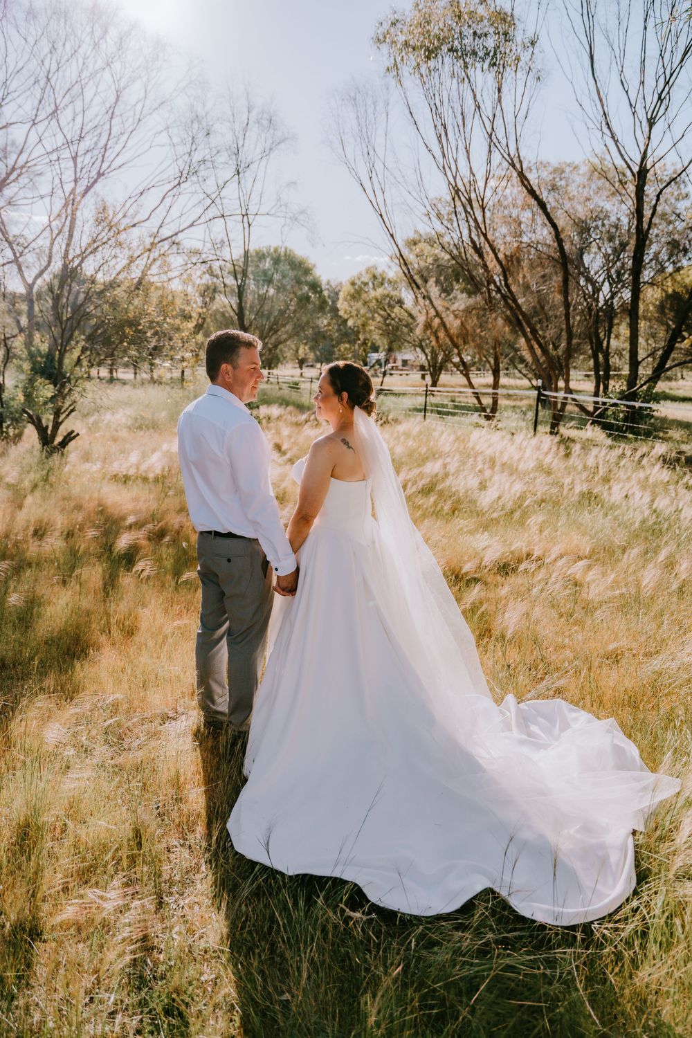 A romantic wedding photoshoot in a sun-lit field with flowing white dress and natural scenery.