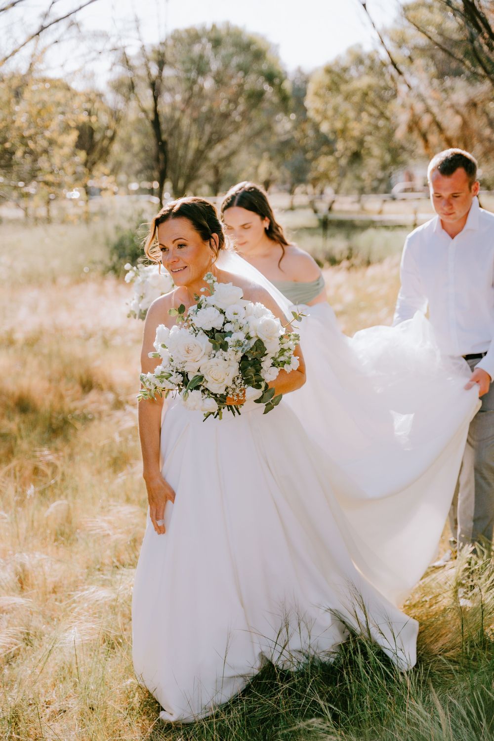 Wedding couple posing in a grassy field with flowing white dress and delicate bouquet.