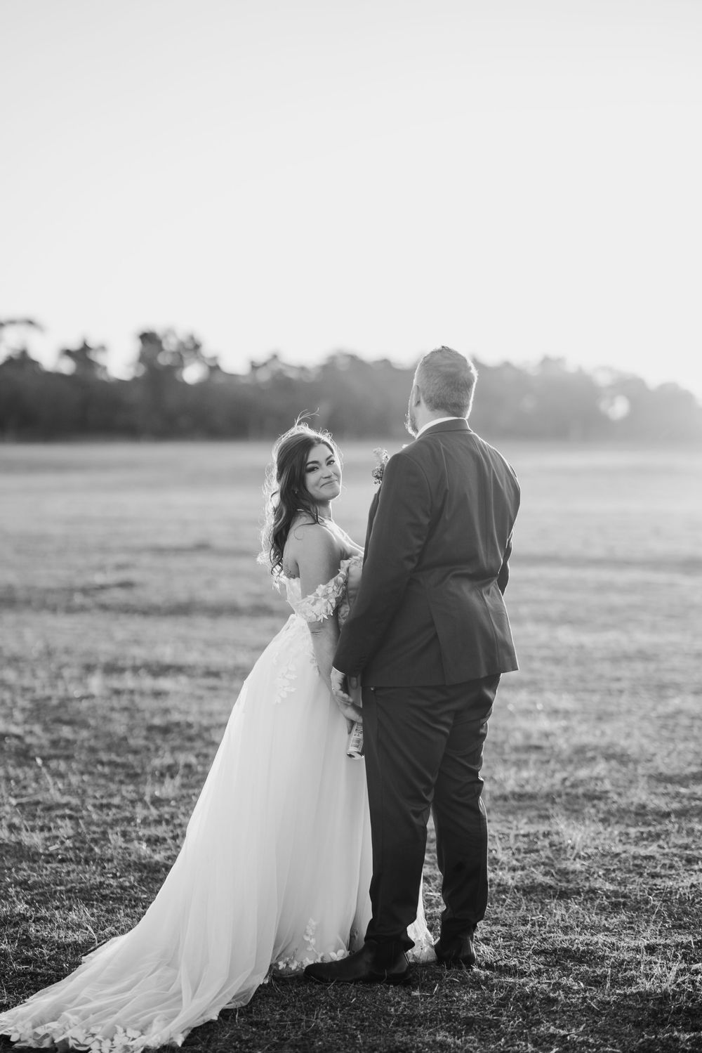 Black and white wedding portrait captured in an open field at dusk.