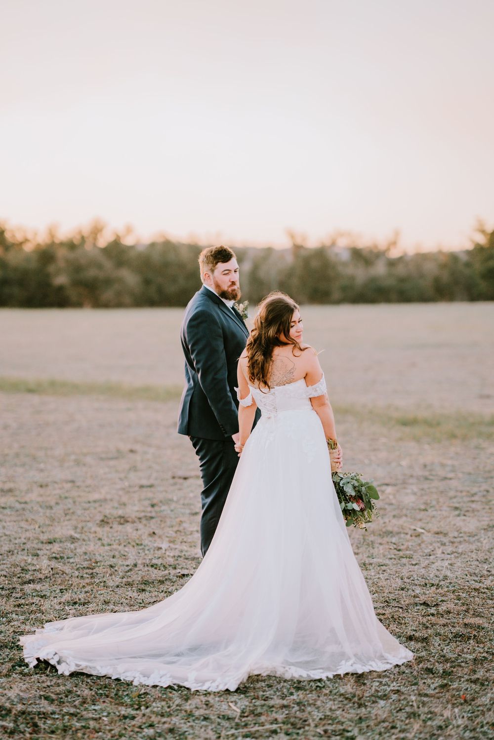 Newlyweds walking together across an open field during golden hour.