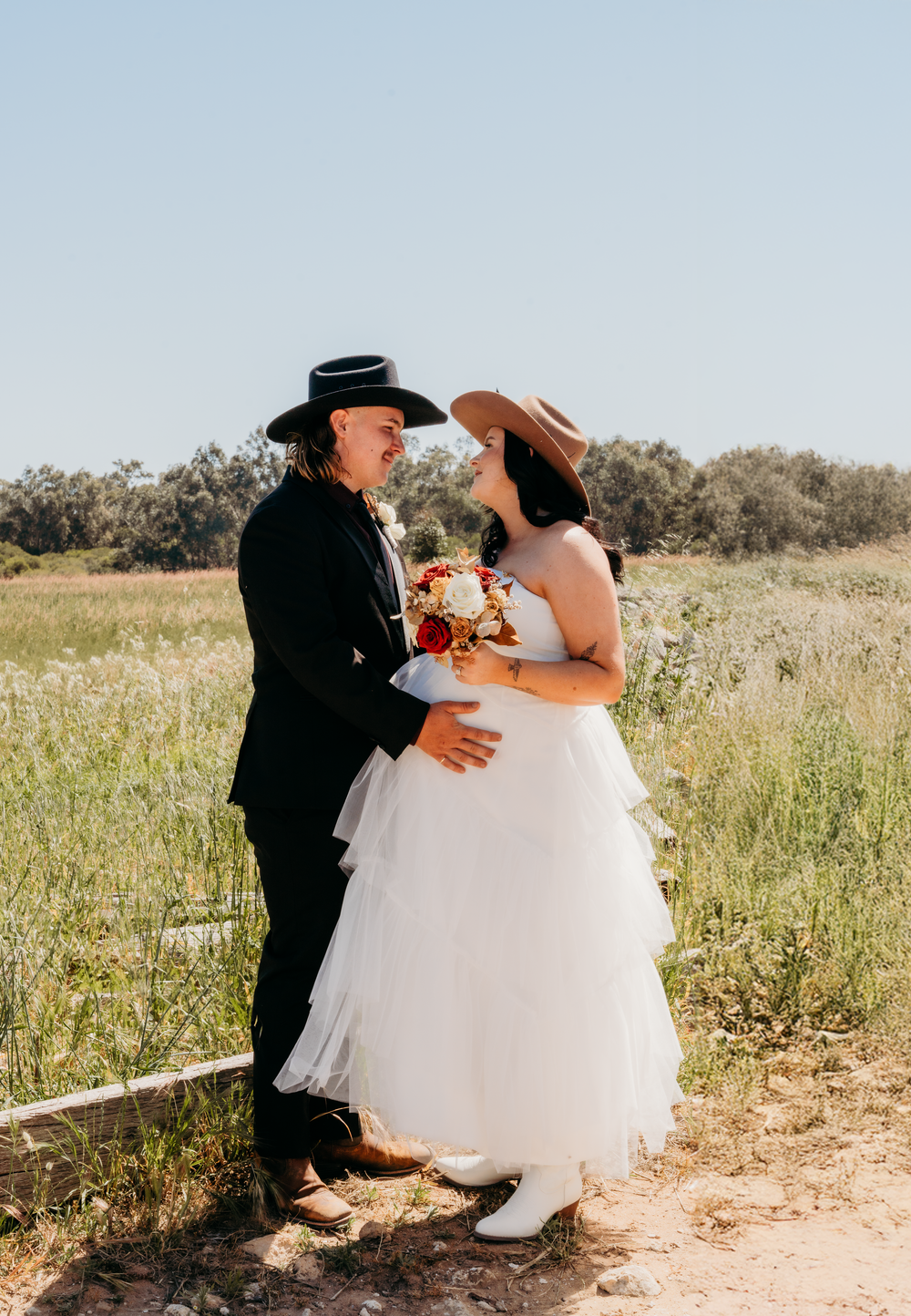 Couple shares intimate moment in western-themed wedding attire outdoors.