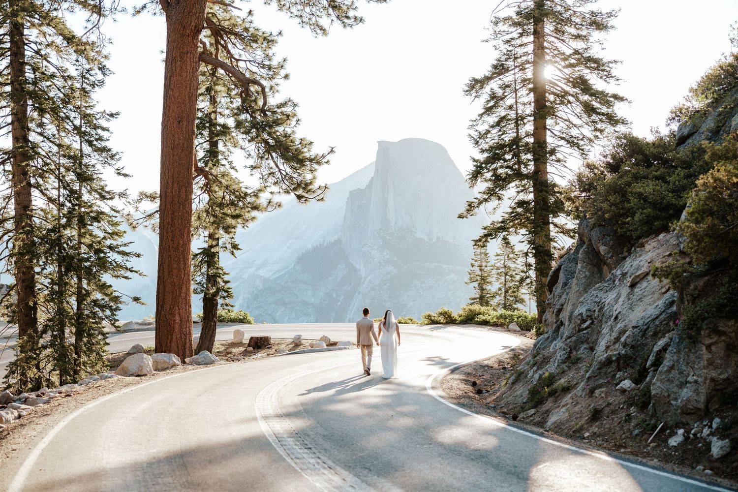 candid photo of bride and groom walking down a road in Yosemite National Park with Half Dome behind them on their elopement day