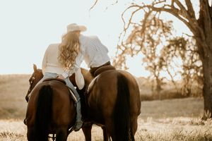 Two riders on horseback sit close together at sunset in a rustic countryside setting.