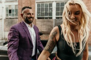 Joyful moment captured with blonde woman and man in purple blazer outside brick building.