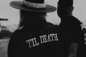 Monochrome closeup of hat worn on someone outdoor in dark lighting with text visible on clothing.
