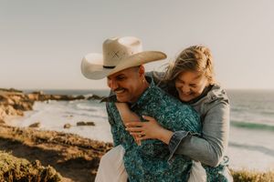 A couple embraces along the rocky coastline during golden hour at the beach with crashing waves in the background.