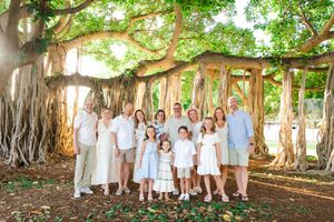 Family portrait session under a majestic banyan tree with multiple groups wearing white clothing in a natural setting.