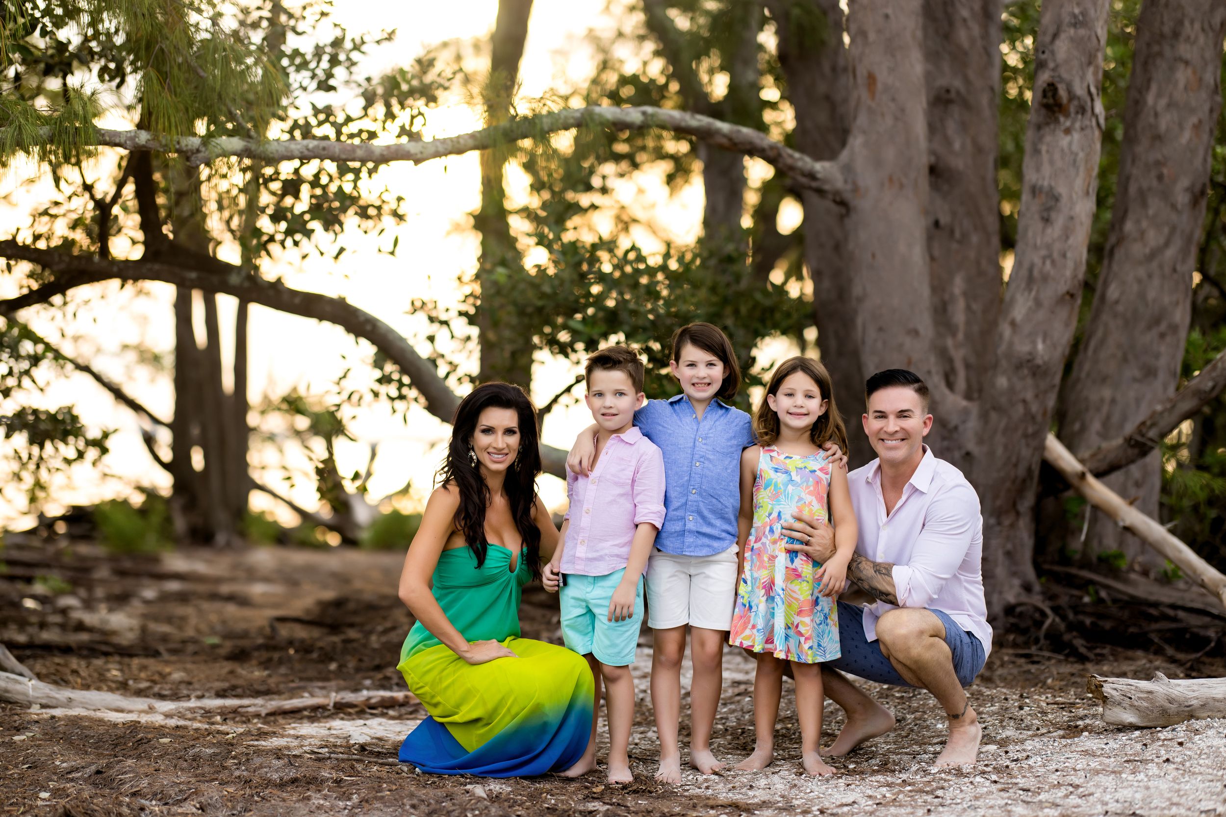 Family group poses together at sunset near large trees.