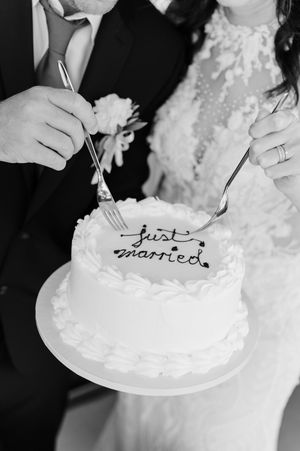 Black and white wedding cake detail shots show someone writing 'just married' in elegant script on a white frosted cake.