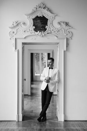 A black and white photo series showing a figure in a white jacket and bowtie posing playfully against ornate doorframes.
