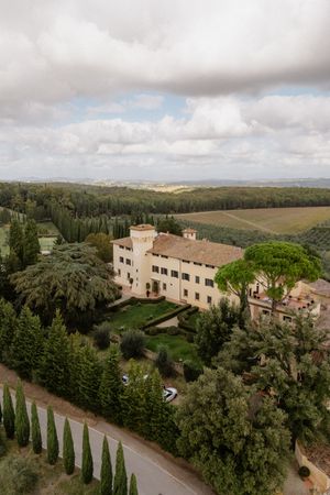 Aerial panoramic view of a Tuscan villa estate nestled among cypress trees and rolling hills in the Italian countryside.