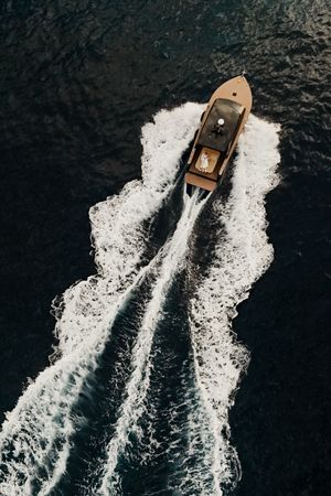 Aerial view of a boat creating white wake patterns in dark ocean waters as it moves forward.