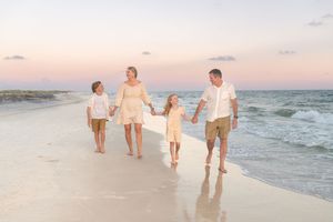 Family group poses together on sandy beach with sea oats and dunes during sunset photo session. Dauphin Island, Alabama