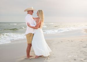 Couple in white posing on the beach during sunset.