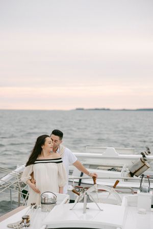 Romantic couple embracing on a luxury yacht at sunset, with calm ocean waters and a soft pastel sky in the background.