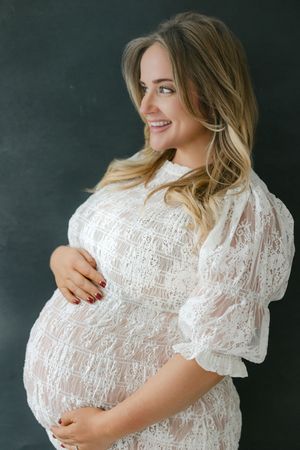 Maternity photos in white lace dress against dark background at the studio showing pregnancy glow | Connecticut Maternity Photographer.