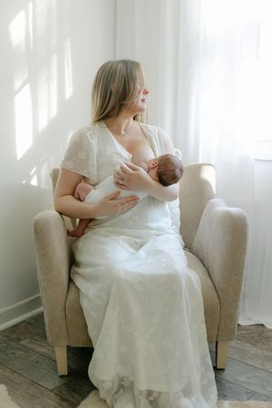 Breastfeeding mom in the studio looking out the window newborn session in Connecticut.