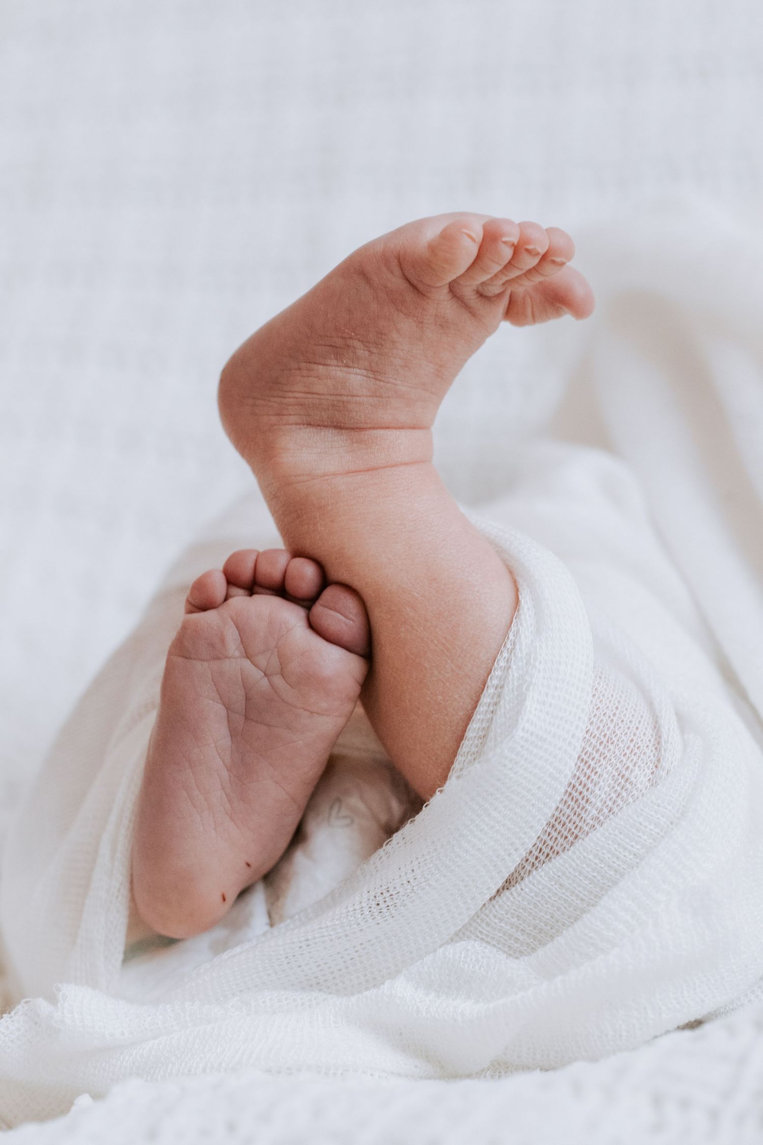 Close-up view of a baby's tiny feet wrapped in soft white fabric on a white textured background.